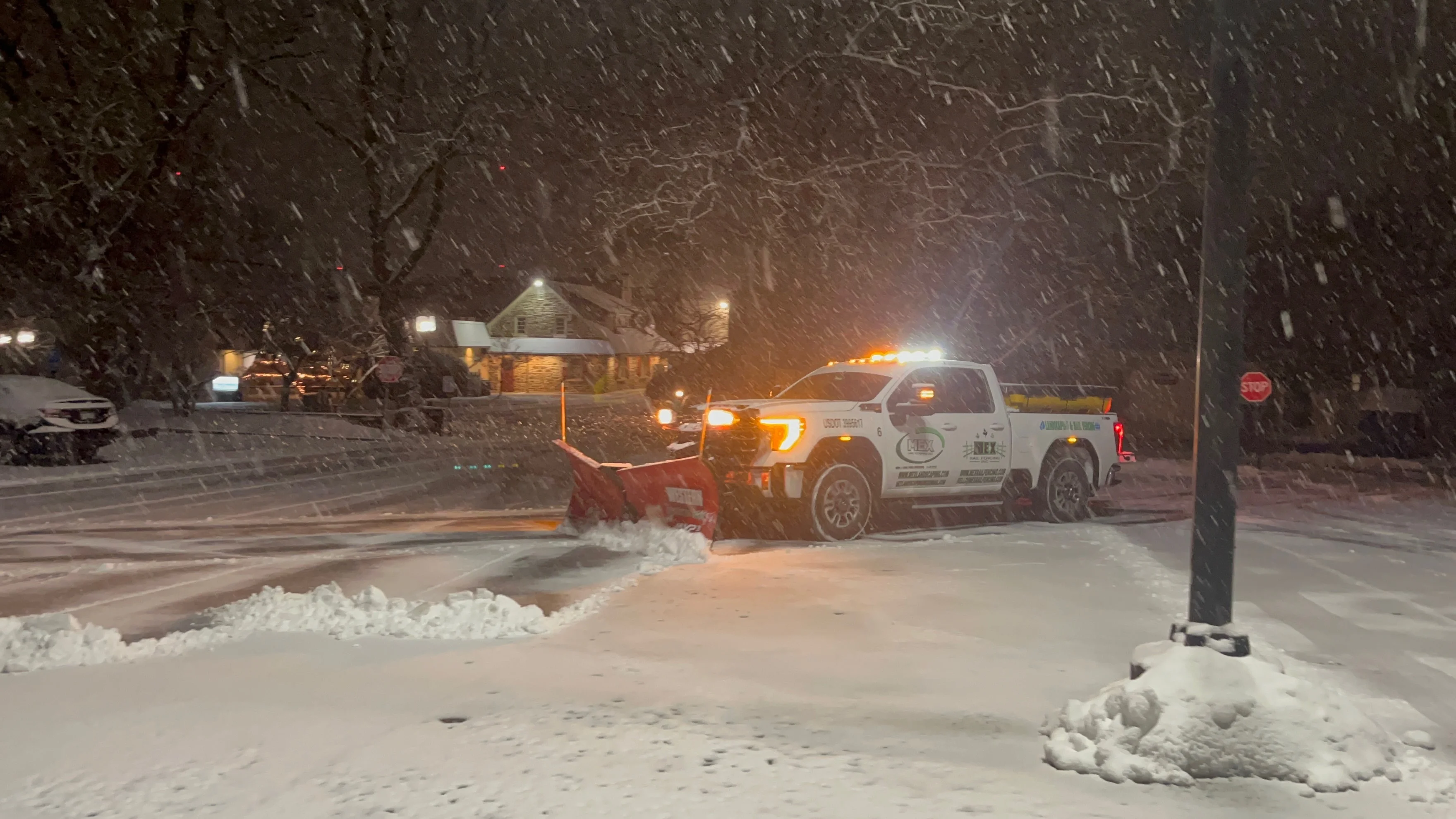 MEX snowplow truck clearing a snow-covered commercial property at night